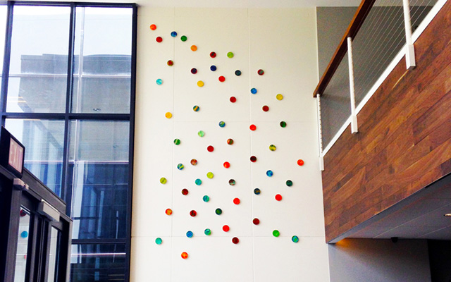 A large art installation of painted wood circles, in a modern office lobby.