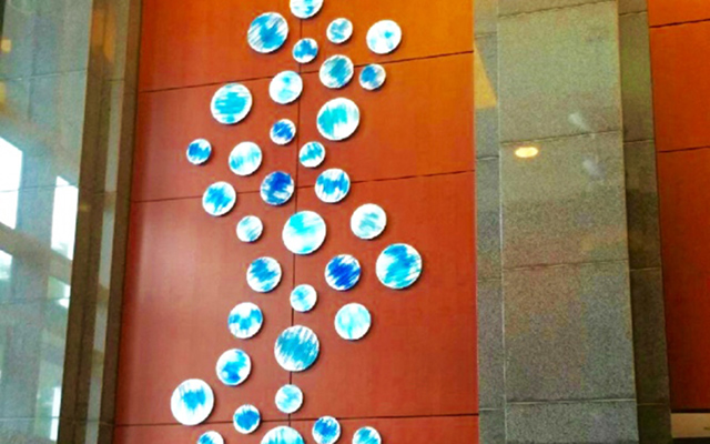 Mini blue paintings on circle pieces, arranged in abstract pattern in corporate lobby